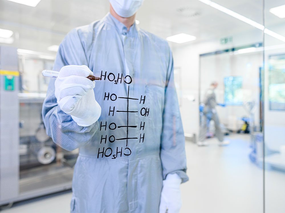 Mitarbeiterin von Domaco in der Produktion, vor einer Glaswand mit einer Formel